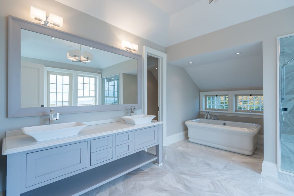 Spa-inspired bathroom design. Large mirror with a double sink. Grey cabinets square lighting. 