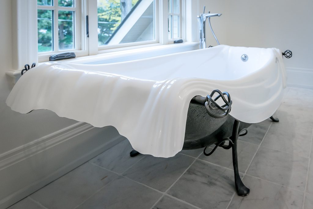 Large flowing porcelain Free Standing Vintage Tub with black metal base sitting in front of a large residential window in a renovated bathroom.